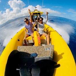 Three people enjoying a ride on a yellow inflatable boat on the ocean.