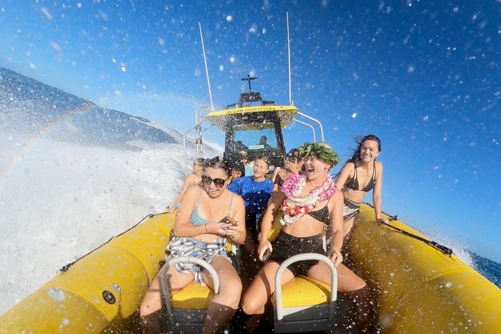 People enjoying a speedboat ride, ocean splashes and a rainbow in the sunny background.