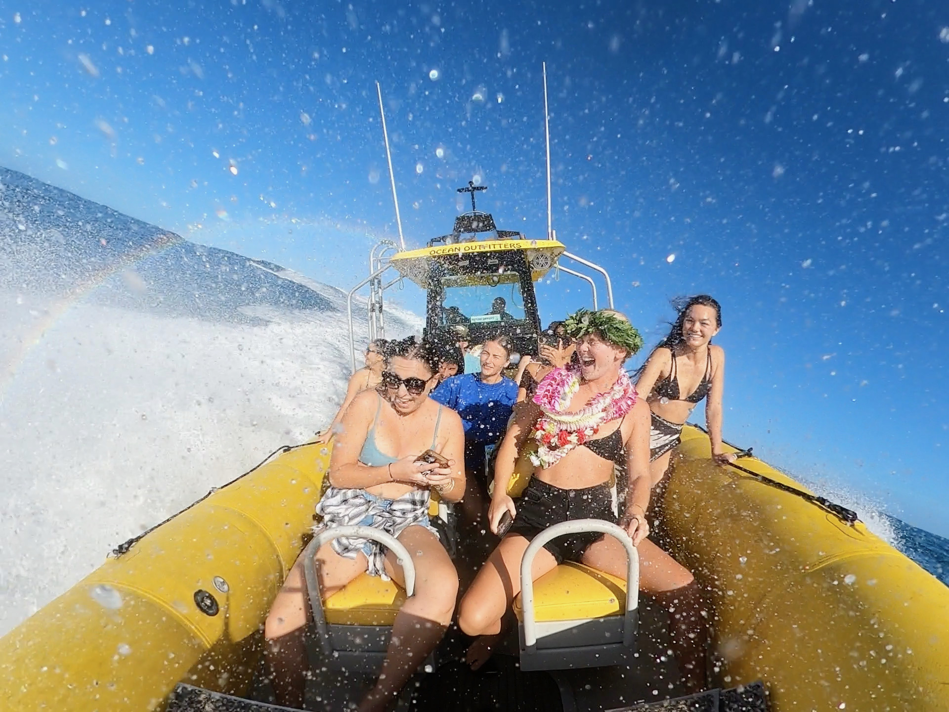 People on a yellow speedboat, enjoying splashes, with a rainbow visible to the side.