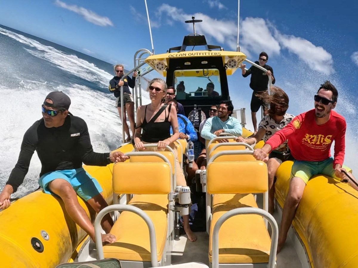 People on a yellow boat ride, splashing through waves under a blue sky.