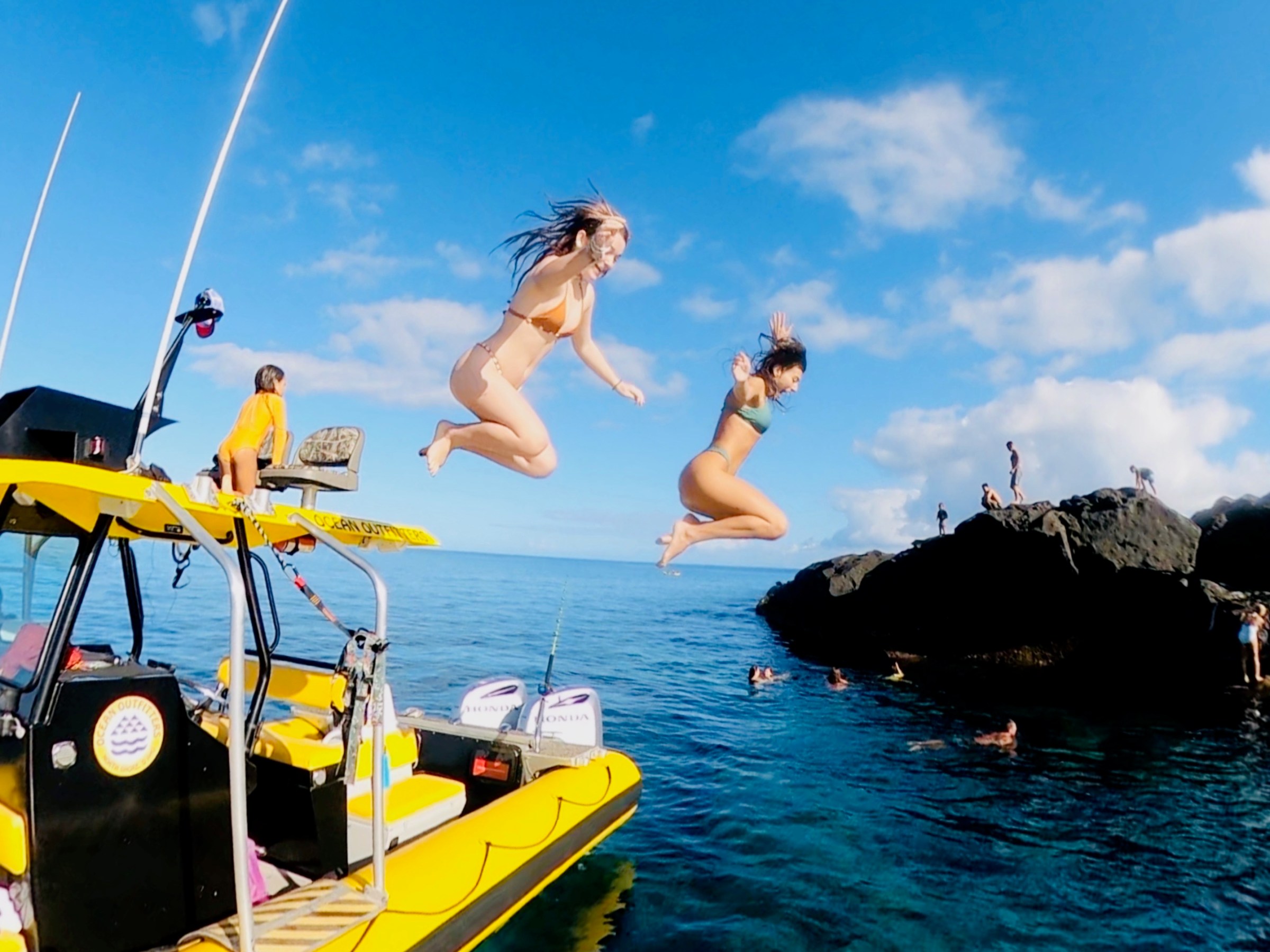 Two people jumping from a yellow boat into clear blue water.