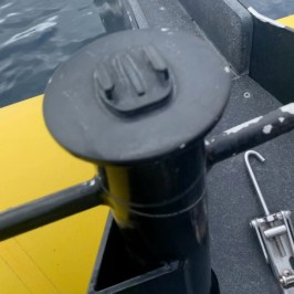 Black boat railing with a mounted rod holder near water.