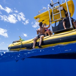 People on a yellow boat, preparing to snorkel in blue ocean under a bright sky.