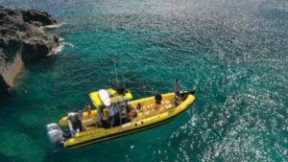 Yellow boat with people on clear blue water near rocky coastline.