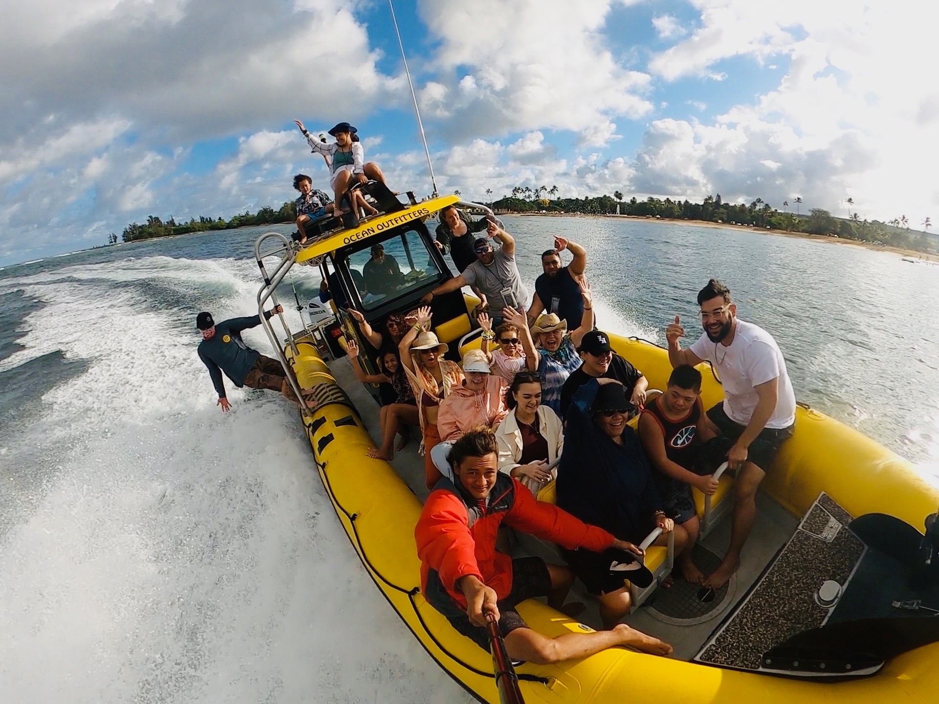 Group of people on a yellow speedboat, smiling with the ocean and coast in the background.