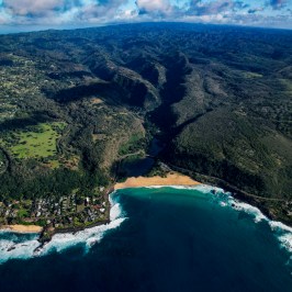 Aerial view of a coastal landscape with mountains, beach, and ocean waves.
