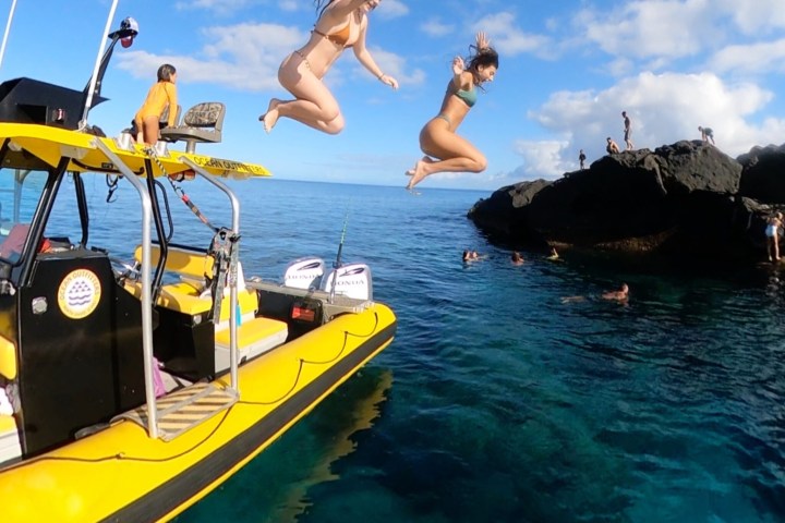 Two people jump from a yellow boat into clear blue water.