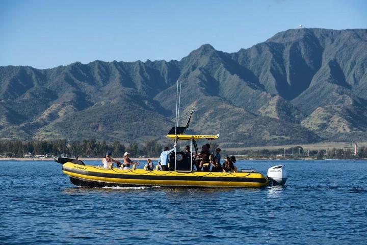 People on a yellow speedboat in the water with mountains in the background.