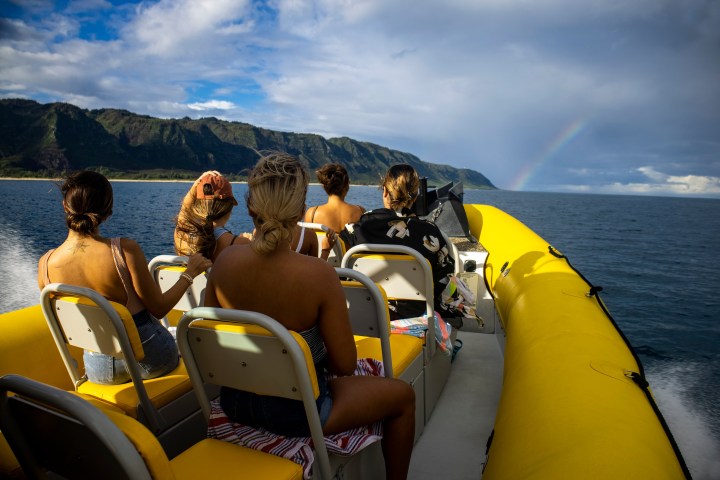 Group on a yellow boat watching a rainbow over the ocean.